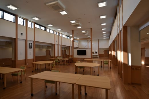 木調で統一された広々とした共用スペース。複数のテーブルと椅子が配置され、採光も良好。