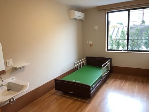 介護施設の居室。ベッド、洗面台、エアコン、窓からの採光が確認できます。