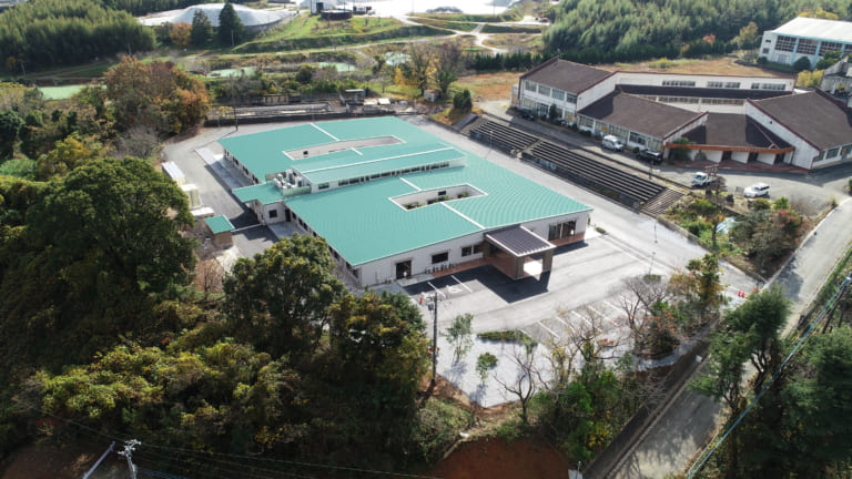 緑色の屋根と広大な敷地を持つ介護施設の航空写真。周辺は豊かな自然環境。